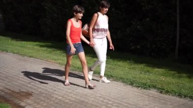 İki kadın, yemyeşil ve canlı bitkilerle çevrili, pitoresk bir yolda yürüyor, sıcak ve güneşli bir günün tadını çıkarıyor birlikte yaşam tarzı ve açık hava aktiviteleri temalarını yakalamak için.