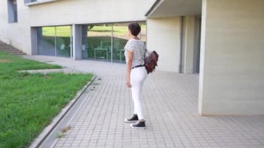 Modaya uygun bir kadın kendine güvenerek ve zarafetle, hareketli modern bir şehir ortamında asfalt bir yolda yürüyor, şık kıyafetlerini ve rahat, yumuşak tavırlarını sergiliyor.