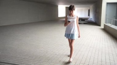 Gündelik, şık giyinmiş genç bir kadın ferah, minimalist bir mimari koridorda rahatça yürüyor. Çağdaş kentsel ortama dalmış bir şekilde telefonuyla meşgul.