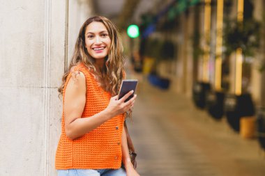 Şehirde telefon kullanan mutlu bir Latin kadının üç çeyrek boyunda fotoğrafı.