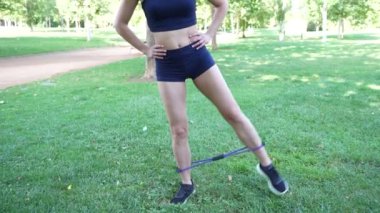 Açık hava parkında, bir kadın bacaklarını güçlendirmek ve güçlendirmek için bir direniş bandı kullanarak bacak kaçırma egzersizlerini etkili bir şekilde sunar. Faaliyet sağlık ve zindeliği teşvik eder.