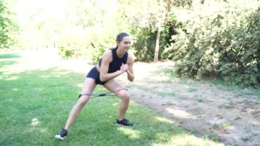 Formda bir kadın, spor yapmak ve spor yapmak için ideal olan barışçıl bir parkta egzersiz yapmak için direniş bantları kullanıyor. Kardiyo, dayanıklılık, esneklik ve bütünsel sağlık için faydalıdır.