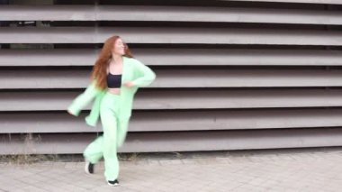 Uzun saçlı neşeli genç bir kadın enerjik bir limon yeşili elbiseyle modern, dokulu bir duvara karşı dans ediyor. Mutluluk ve özgürlüğü ifade ediyor. Sahne enerji ve neşe yayar.