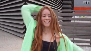 Canlı genç bir bayan açık havada neon yeşil bir kıyafetle coşkuyla dans ediyor, dinamik hareketler ve neşeli bir gülümseme sergiliyor, gençlik enerjisinin canlı ve neşeli bir ifadesini yansıtıyor.