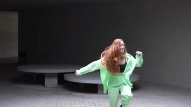 Moda bir şehir ortamında, canlı kızıl saçlı şık neon yeşil giysiler içinde enerjik bir şekilde dans eden, dinamik hareketler sergileyen ve büyüleyici bir performans sergileyen şık bir kadın...