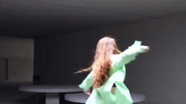 Canlı modern bir dansçı, yeşil kıyafetlerle süslenmiş, çarpıcı kızıl saçlar, dinamik ve enerjik bir performans sergiliyor, minimalist bir arkaplana karşı zarif hareketlerle dolu.