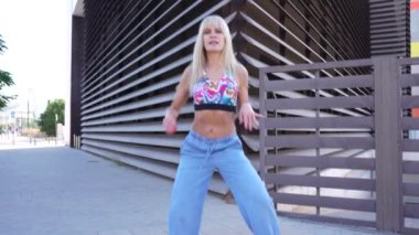 Kendine güvenen sarışın kadın modern mimariye karşı açık havada poz verirken şık ve modaya uygun bir hava yayıyor. Onun genç ve enerjik görünümü onun şık kıyafetleri tarafından geliştirilmektedir.