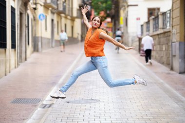 Şehirde zıplayan ve kollarını açan Latin bir kadının tam boy portresi.