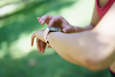 Parkta, bir kadın spor için teknolojiyi kucaklıyor, akıllı bir kaset takıyor. Çevreci bir ortamda sağlıklı bir yaşam için dijital aletler kullanıyor. Modern teknolojiyi egzersizle birleştiriyor.