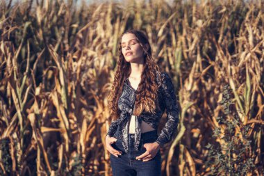 Uzun mısır saplarının arasında zarif bir şekilde duran bir kadının doğal güzelliğini ve zarafetini sergilediği huzurlu bir an.