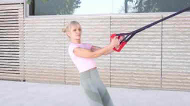 Pembe bluzlu bir kadın vücudunun üst kısmını güçlendirmek için açık havada direnç bandı egzersizi yapıyor. Uygun tekniğin önemini gösterir.