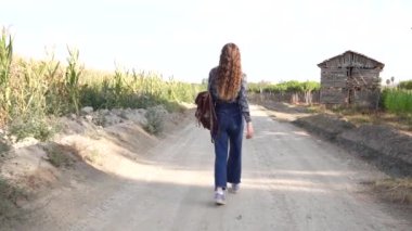 Genç bir kadın, canlı yeşillik ve kırsal ahşap yapılarla dolu huzurlu toprak bir yolda yürüyor, özgürlüğü somutlaştırıyor ve çevresindeki güzel doğayla derin bir bağ kuruyor.