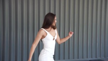 Kendine güvenen bir model, izleyicileri görsel çekiciliğiyle büyüleyen zarif ve çağdaşlık saçan, dokulu gri bir arka plan karşısında büyüleyici bir beyaz elbise sergiliyor.