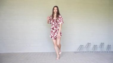 Neşeli bir kadın, çiçekli bir elbiseyle basit bir arkaplana karşı anlamlı bir şekilde dans eder. Canlı enerji ve zarafet saçar. Her hareketinde bireyselliğini ve kutlama ruhunu sergiler.