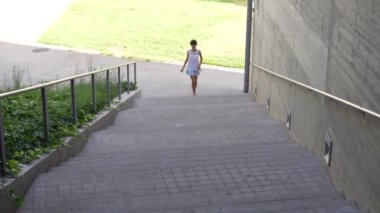 Genç bir çocuk neşeyle, hayat dolu ve modern bir kentsel ortamda parlak, güneşli bir günü temsil eden yeşilliklerle çevrili bir dizi açık hava merdiveninden iner.