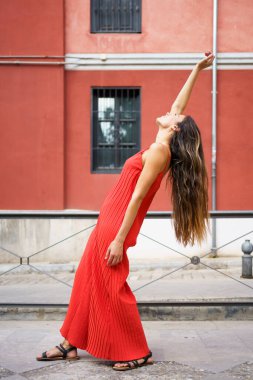 Şık ve zarif bir kadın akıcı, göz kamaştırıcı kırmızı bir elbise içinde çarpıcı ve çarpıcı bir poz veriyor çarpıcı, çarpıcı güzelliğini artıran renkli bir arka plana karşı.