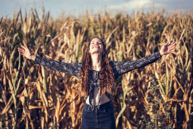 A joyful woman stands gracefully in a vast cornfield, her arms wide open and outstretched, celebrating the beauty of nature and the sense of freedom that comes with it under a clear, bright blue sky clipart