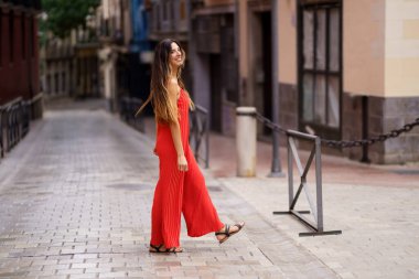 A stylish woman strolls with effortless grace down a charming city street, her vibrant red outfit radiating confidence and elegance, drawing the eyes of everyone around her with each step she takes clipart