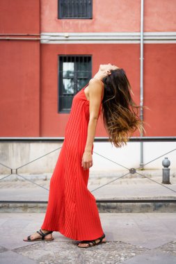 Göz kamaştırıcı kırmızı bir elbise giymiş genç bir kadın zarif bir poz veriyor canlı ve renkli bir arkaplanda, zarif bir şekilde hareket ederken zarafetini ve güzelliğini mükemmel bir şekilde gösteriyor.