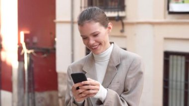 Zarif bir şekilde şık giyinmiş profesyonel bir kadın, akıllı telefonuyla açık havada etkileşime geçiyor, günümüzde dijital çağda modern iletişimin özünü gösteriyor.