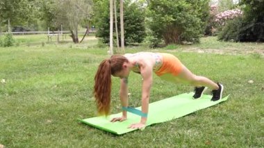 Açık havada sakin bir ortamda kararlı bir kadın yoga minderinde zorlu bir kalas egzersizi yaparak gücünü gösteriyor. Form ve dayanıklılık seviyesini vurguluyor.