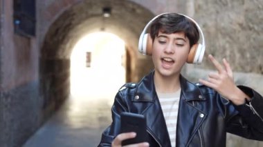 Şık kulaklıklar takan ve modaya uygun deri ceket giyen genç bir insan, akıllı telefonunda müzik dinlemekten keyif alırken, aynı zamanda büyüleyici ve canlı bir açık hava ortamı yaratıyor.