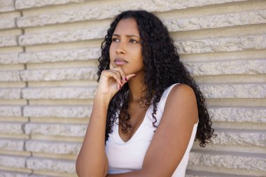 Güzel kıvırcık saçlarıyla karakterize olan genç bir kadın, düşünceli bir şekilde dokulu bir duvara karşı poz verir. Bu da, o anda içsel düşüncelerini ve duygularını derin bir şekilde yansıttığını gösterir.