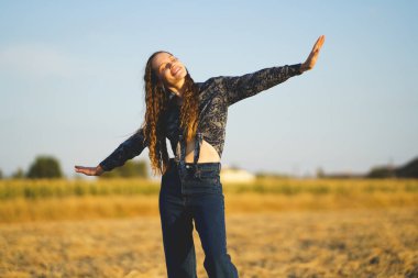 Neşeli bir kadın altın bir alanda dans eder. Canlı bir günbatımının keyfini çıkarırken özgürlük ve mutluluğu somutlaştırır. Enerjisi ve ruhuyla anı güçlendirir.