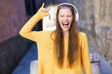 Parlak sarı bir süveter giyen, şık kulaklıklar takan genç bir kadın kendini müziğe daldıkça neşeyle ifade ediyor. Çevresindeki canlı şehir atmosferini tamamen kucaklıyor.
