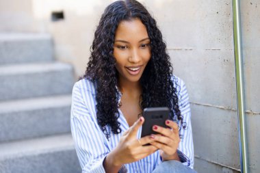 Heyecanlı ve zeki telefonuna odaklanmış genç bir kadın, merdivenlerde ustalıkla geziniyor, modern teknolojinin günlük hayatı ve sosyal etkileşimleri üzerindeki önemli etkisini gösteriyor.