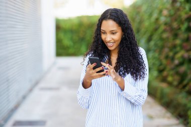 Kıvırcık saçlı neşeli genç bir kadın akıllı telefonuna odaklanırken etrafını çarpıcı yeşil manzaralar sarar. Bu da neşesine neşe katar ve kaygısız ruhunu ve hayat dolu tavırlarını güçlendirir.