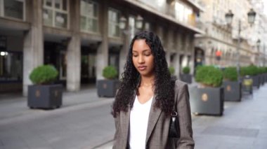 Şık, modaya uygun, güzel kıvırcık saçlı genç bir kadın modern bir şehir manzarasında rahatça geziniyor. Olağanüstü moda anlayışını ve doğal zarafetini zahmetsizce sergiliyor.