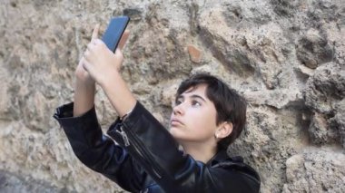 Şık deri ceketli hayat dolu bir şehirde selfie çeken hayat dolu genç bir insan, modern gençlik kültürünün, yenilikçi modanın ve etraflarındaki kesici teknolojinin karışımını yansıtıyor.
