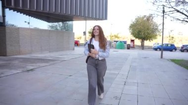 Kendine güvenen bir kadın kasıtlı olarak modern bir binanın dışında yürüyor, bir klasörü tutuyor ve işyerindeki başarıyı ve kişisel başarıyı her adımda somutlaştıran sıcak bir gülümseme yayıyor.