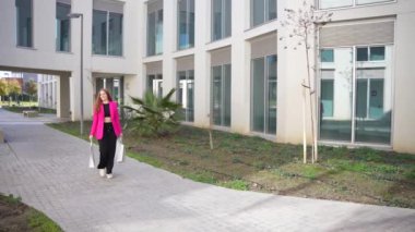 Kendine güvenen bir kadın, bereketli yeşillik ve parlak cam binalarla çevrili modern mimari bir yolda yürüyor. Bölgenin canlı kentsel tasarımı ve yaşam tarzını gözler önüne seriyor.