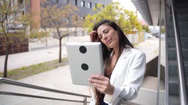 Kendine güvenen bir kadın şehir ortamında elinde modern teknolojiyi gösteren bir tablet tutarak şık görünüşünü, çevresiyle kusursuz bir şekilde harmanlıyor.