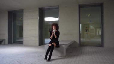 Minimalist bir alanda, derin düşüncelere dalmış genç bir kadın akıllı telefonunu tutarak modern yaşam tarzını, dijital bağlantıyı ve kişisel yansımasını sembolize ederek çağdaş yaşamı yakalıyor.