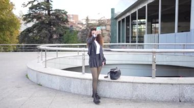 Genç bir kadın rahat ve rahat bir poz verir, akıllı telefonunu kullanırken şehir ortamında modern bir yaşam tarzını ve günlük hayatımızda iletişimin önemini gözler önüne serer.