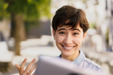 Neşeli genç bir kadın, tabletleriyle uğraşırken, dijital dünyadaki modern hayatımızı tanımlayan mutluluğu, bağlantıyı ve coşkuyu gösteren parlak bir şekilde gülümsüyor.