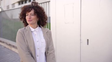 Şehir sahnesinde kıvırcık saçlı neşeli bir kadın neşeli bir şekilde elinde moda ve mutluluğu yansıtan renkli alışveriş çantaları tutuyor, gittiği her yere ışık saçıyor.