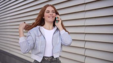 Canlı bir şehir ortamında, uzun kızıl saçlı şık genç bir kadın şık yaşam tarzını yansıtan moda kıyafetlerini sergileyerek canlı bir telefon görüşmesi yapıyor.