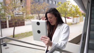 Zarif bir beyaz ceket giymiş kendine güvenen bir kadın, parlak ve güneşli bir günde tabletiyle etkileşime geçiyor ve modern teknolojinin günlük hayatta ve işte nasıl kullanıldığını gösteriyor.