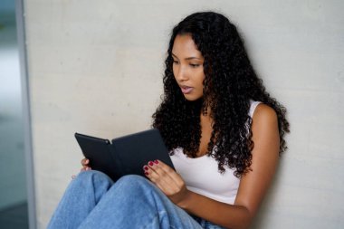 Genç bir kadın rahatça oturuyor, kitabıyla meşgul, boş aktivitelerin ideal temaları, modern okuma sanatı ve teknolojinin günümüz yaşam tarzındaki rolünü somutlaştırıyor.