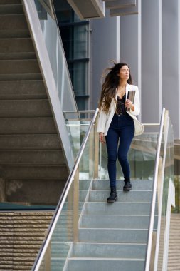 Şık ve şık genç bir kadın modern bir merdiven iniyor, şehir mimarisinin çarpıcı güzelliğini ve çağdaş tasarım estetiğinin inceliklerini gösteriyor.