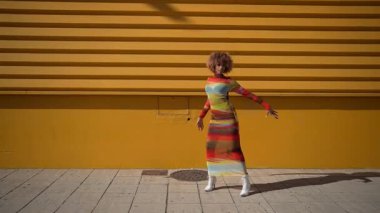 Modaya uygun bir model, parlak sarı bir duvara karşı canlı çizgili bir elbise sergiliyor. Çevresindeki şehri çevreleyen canlı şehir atmosferini ve enerjik atmosferi mükemmel bir şekilde yakalıyor.