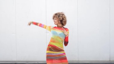 Canlı bir elbise giymiş enerjik bir dansçı büyüleyici bir duruş sergiliyor. Zarif hareketlerini minimalist beyaz bir arka plana karşı sergiliyor. Bu zıtlığı arttırıyor ve dikkat çekiyor.