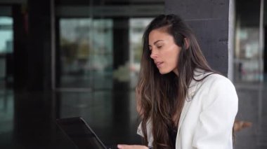 Şık ve şık giyinmiş bir kadın şık ve modern bir çalışma alanında rahat bir şekilde oturur, bilgisayarına derinden odaklanır, bugün uzaktan çalışmanın çağdaş eğilimlerini etkili bir şekilde gözler önüne serer.