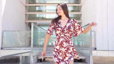 Mimari olarak tasarlanmış basamaklarda kendine güvenen şık genç bir kadın şık bir açık hava ortamında şık desenli elbisesini sergiliyor, ılık gün ışığında güzelce yıkanmış.