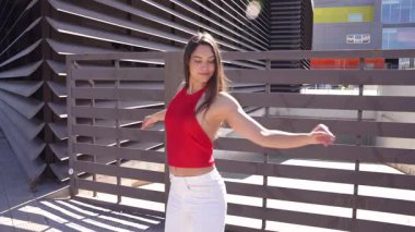 Zarif, kendine güveni ve zarafeti olan şık beyaz şortuyla çarpıcı kırmızı bir bluz giyen şık bir kadın göz alıcı bir arka fona karşı zarafetle poz veriyor.