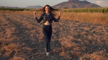 Genç bir kadın güneşli, geniş, çorak bir arazide direnç ve özgürlük duygusunu temsil ederken nefes kesici ve güzel bir günbatımı arka planına karşı çerçevelenmiş bir şekilde duruyor.